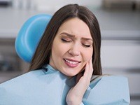Woman in dental chair holding cheek