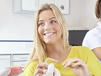 Smiling woman in dental chair holding Invsialign tray