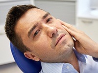 Man in dental chair holding cheek