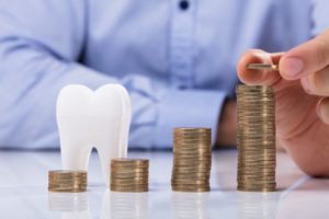 Midlothian dentist with model tooth and increasing stacks of coins
