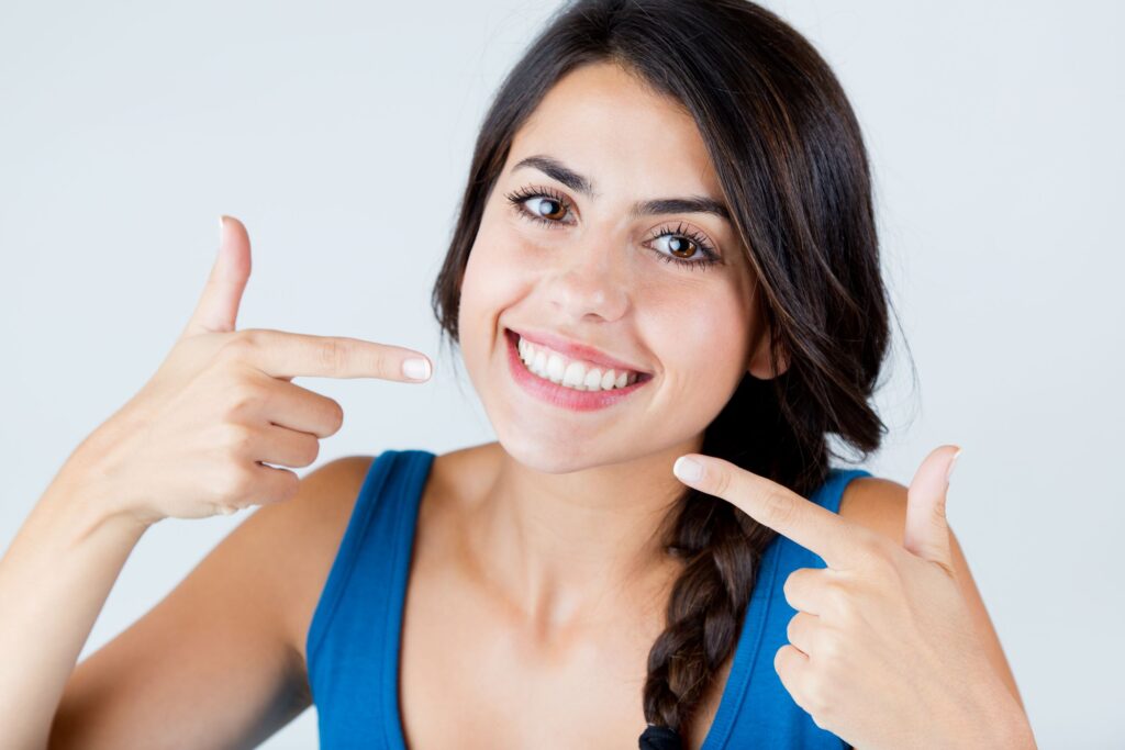 Woman in blue shirt pointing to her beautiful smile with both hands