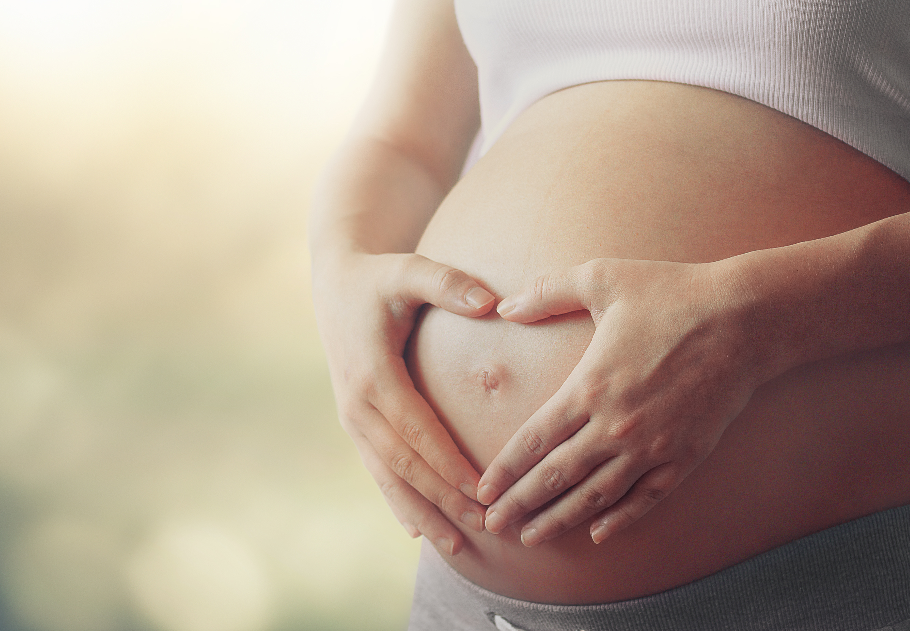 Woman holding pregnant belly with hands in a heart shape.
