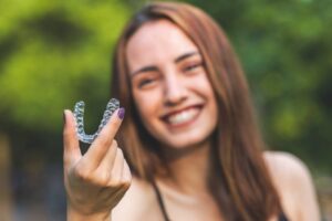 Woman smiling and holding up her Invisalign tray